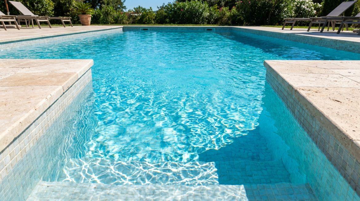 Vue rapprochée d'une piscine rectangulaire à l'eau turquoise cristalline, avec des marches et des bords en pierre claire.