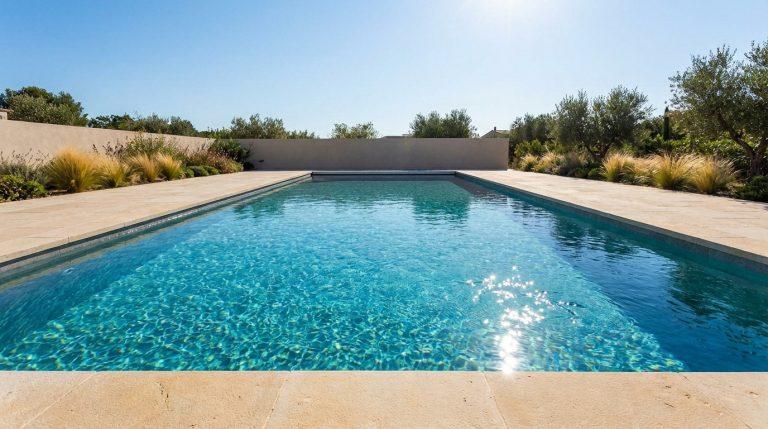 Piscine rectangulaire extérieure, eau turquoise scintillante sous le soleil, entourée de pavés clairs et de verdure méditerranéenne.