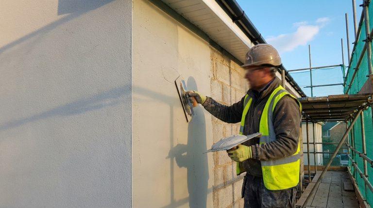 Un ouvrier façadier appliquant manuellement de l'enduit ciment sur un mur extérieur en blocs, avec truelle et taloche.