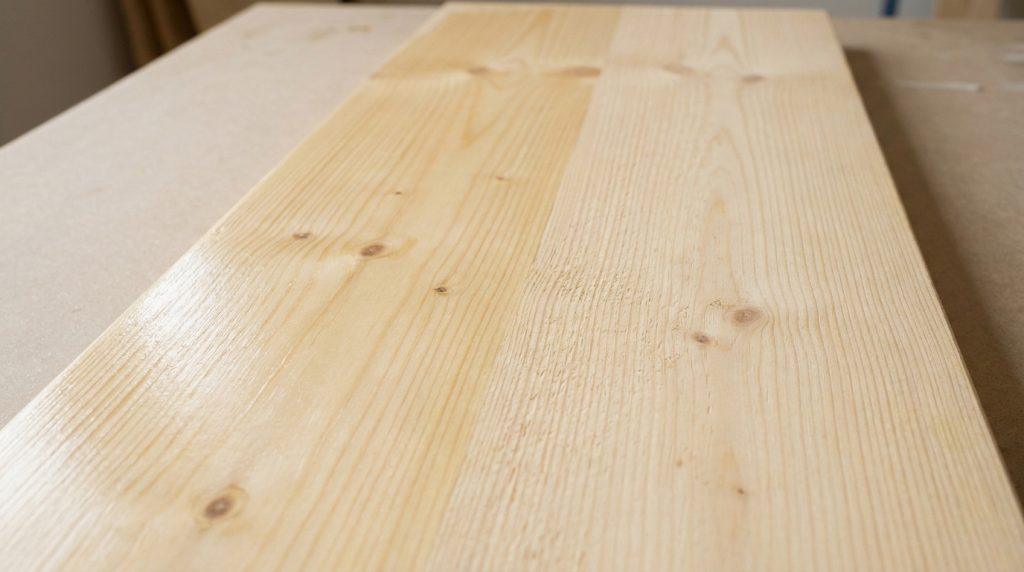 Une planche de bois clair montrant une différence de texture et de reflet entre une zone traitée et une zone brute.